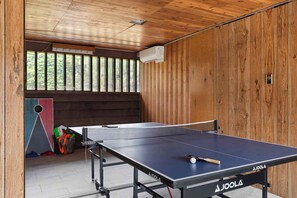 A ping pong table with a net, a paddle, and a ball in a room with wooden walls and a window. - RetroRetreat on the Preserve | Dunes/Games/FirePit (South Haven)