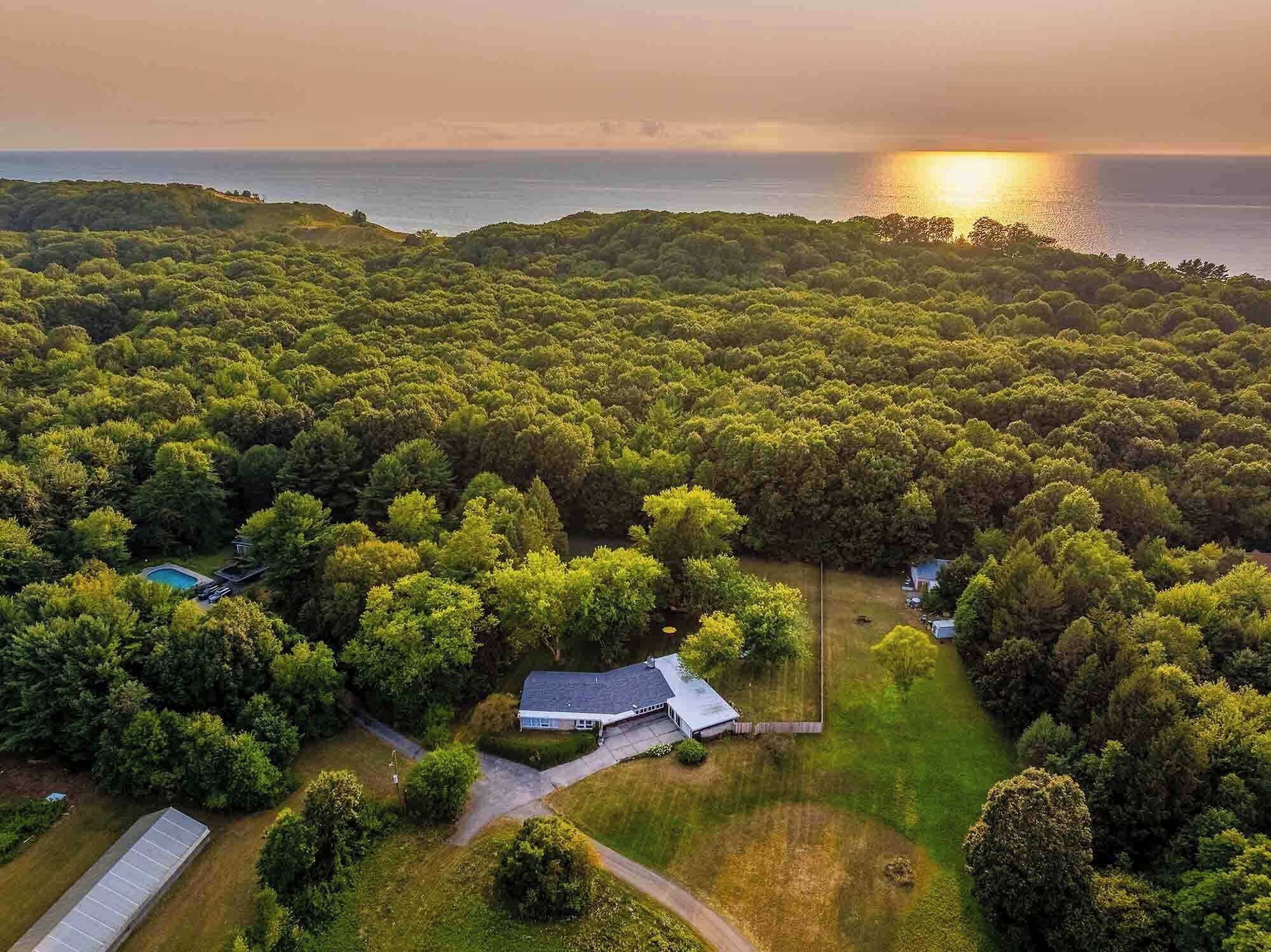 Ein Wohngebiet mit einem Haus, umgeben von üppiger Bepflanzung, einem Schwimmbad und Blick auf den Ozean bei Sonnenuntergang.