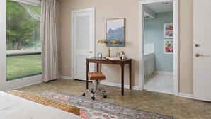Una camera d'albergo con un'ampia finestra, una scrivania con una sedia, un tappeto e una porta che dà accesso al bagno.