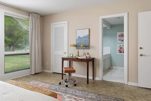 A hotel room with a large window, a desk with a chair, a rug, and a door leading to a bathroom. - RetroRetreat on the Preserve | Dunes/Games/FirePit (South Haven)