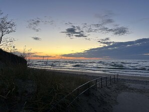 A beach with a metal railing, waves, and a sunset.