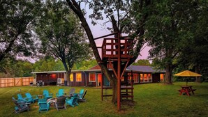 A backyard with a fire pit, outdoor seating, and a treehouse structure.