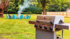 A barbecue grill with controls, a grill cover, and a chimney emitting smoke.