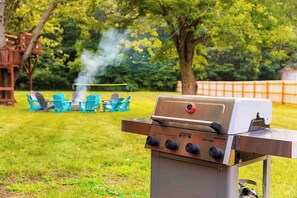 A barbecue grill with controls, a grill cover, and a chimney emitting smoke.