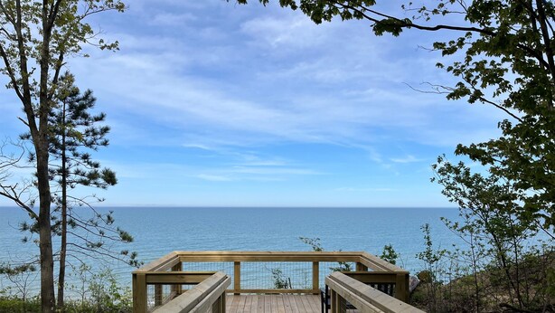 A wooden deck leading to a beach with a clear view of the ocean.