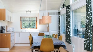 Una cocina moderna con armarios blancos, una mesa de comedor con sillas y un amplio ventanal con vista a zonas verdes.