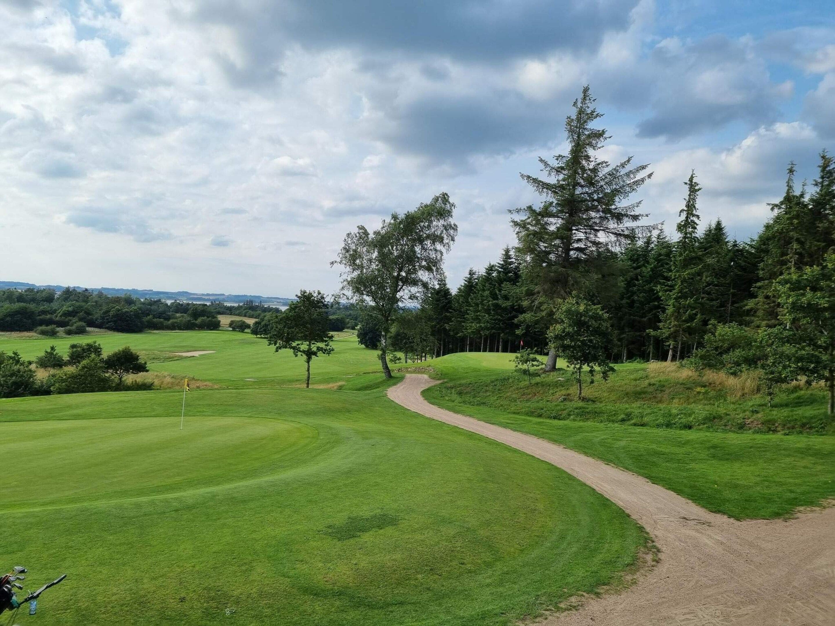 A golf course with a winding dirt path, surrounded by trees and open grassy areas.