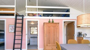 Un cuarto tipo loft con una escalera de madera, una mesa de comedor con sillas, un armario y una lámpara colgante.
