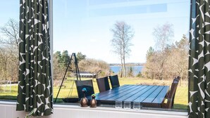 Un comedor con mesa y sillas, vista a un lago, y una ventana con cortinas estampadas.