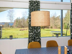 A dining area with a view of a grassy field and trees, a wicker lamp, patterned curtains, and a table with chairs. - 7 Person Holiday Home in Skals (Skals)