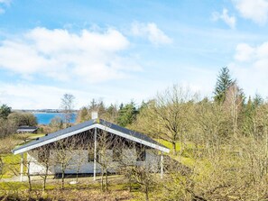A modern house with a sloped roof, surrounded by trees and a body of water in the background. - 7 Person Holiday Home in Skals (Skals)