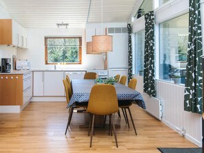A modern kitchen with white cabinets, a dining table with chairs, and a window with blinds. - 7 Person Holiday Home in Skals (Skals)