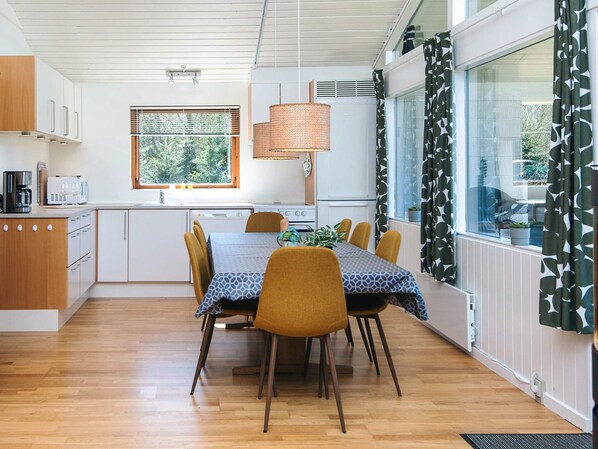 Una cocina moderna con armarios blancos, una mesa de comedor con sillas y una ventana con persianas.