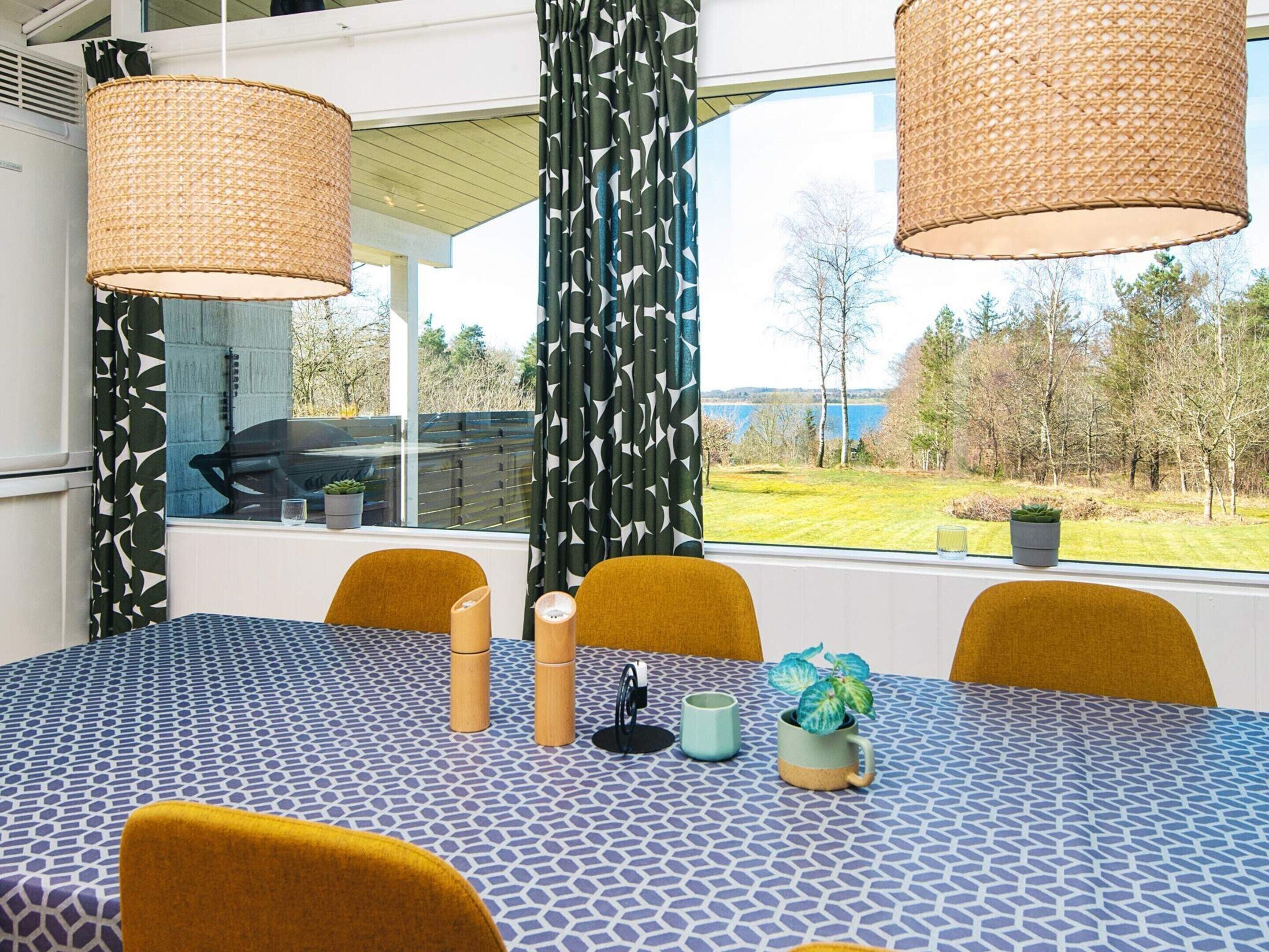 A dining area with a patterned tablecloth, yellow chairs, and a view of a lake through large windows.