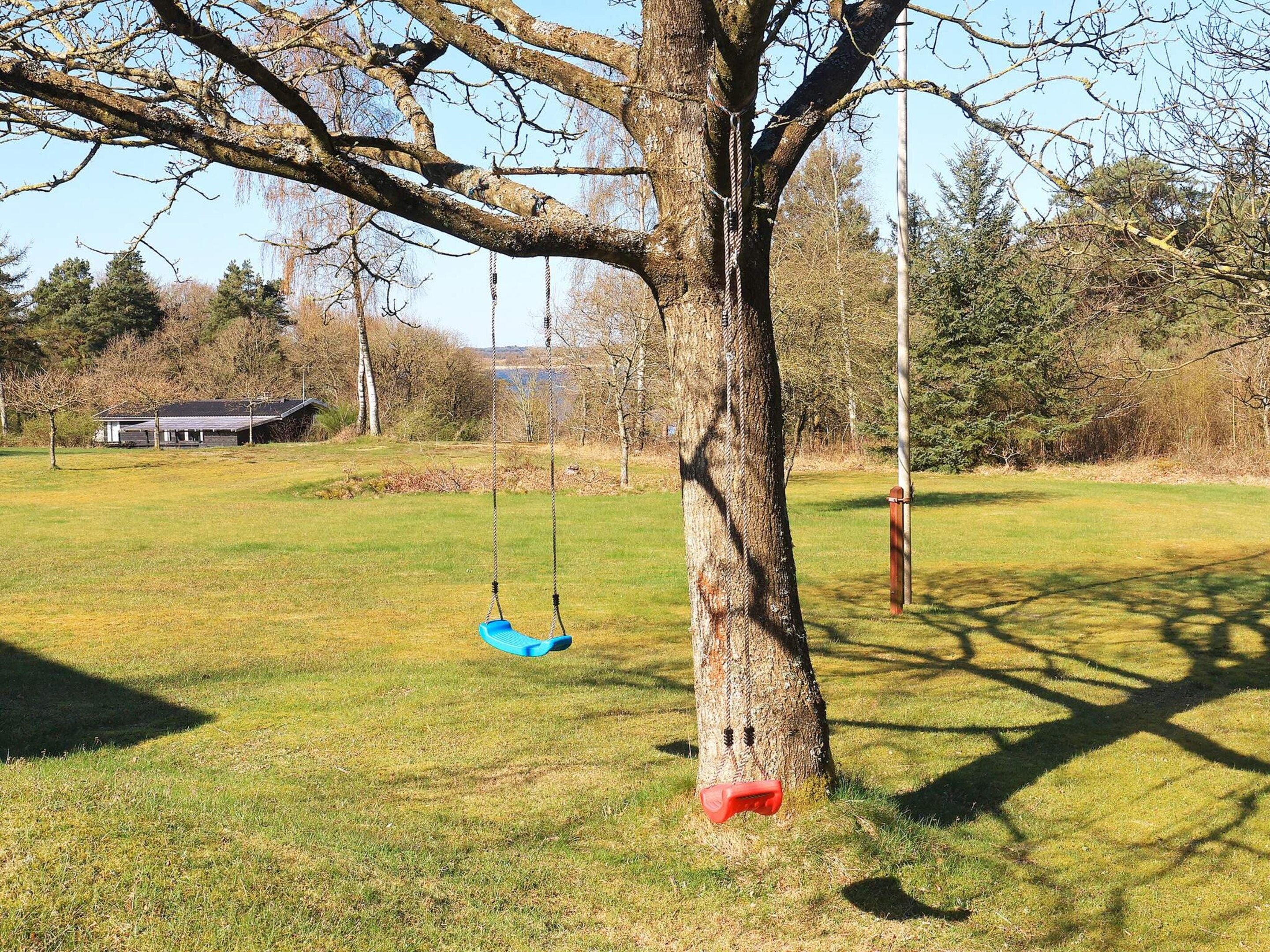 Ein Baum mit einer Hängematte, eine grüne Wiese und ein Gebäude im Hintergrund.