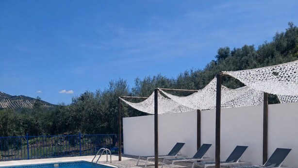 En swimmingpool med ett vitt trädäck, solstolar och en vit pergola.