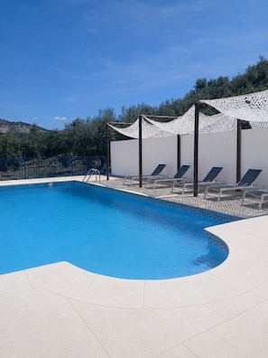 Ein Swimmingpool mit weißer Liegefläche, Liegestühlen und einer weißen Pergola.