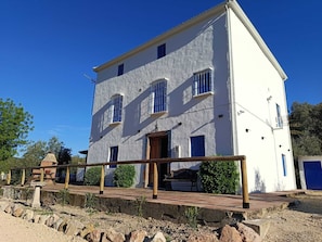 A two-story building with a balcony, a wooden deck, and a stone wall in the foreground. - Rural house located in the heart of the Natural Park of the Sierras Subbeticas. (AN)