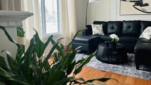 A modern living room with a black leather sofa, a round black coffee table, and a large window with curtains.