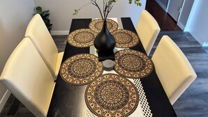 A dining table with a black and gold patterned table runner, four chairs, and a vase with a branch.