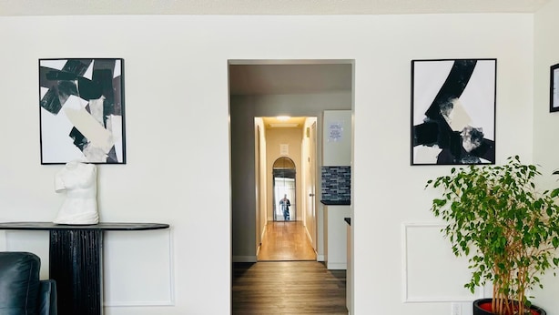 A hallway with wooden flooring, a black leather sofa, a white bust sculpture, and abstract art on the walls.