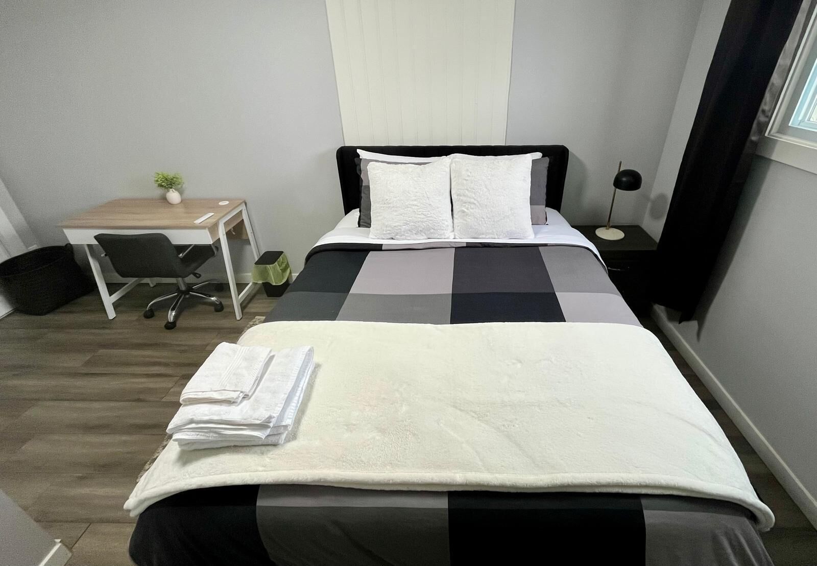 Une chambre d’hôtel bien rangée, avec un lit, un bureau, une chaise et une petite table.