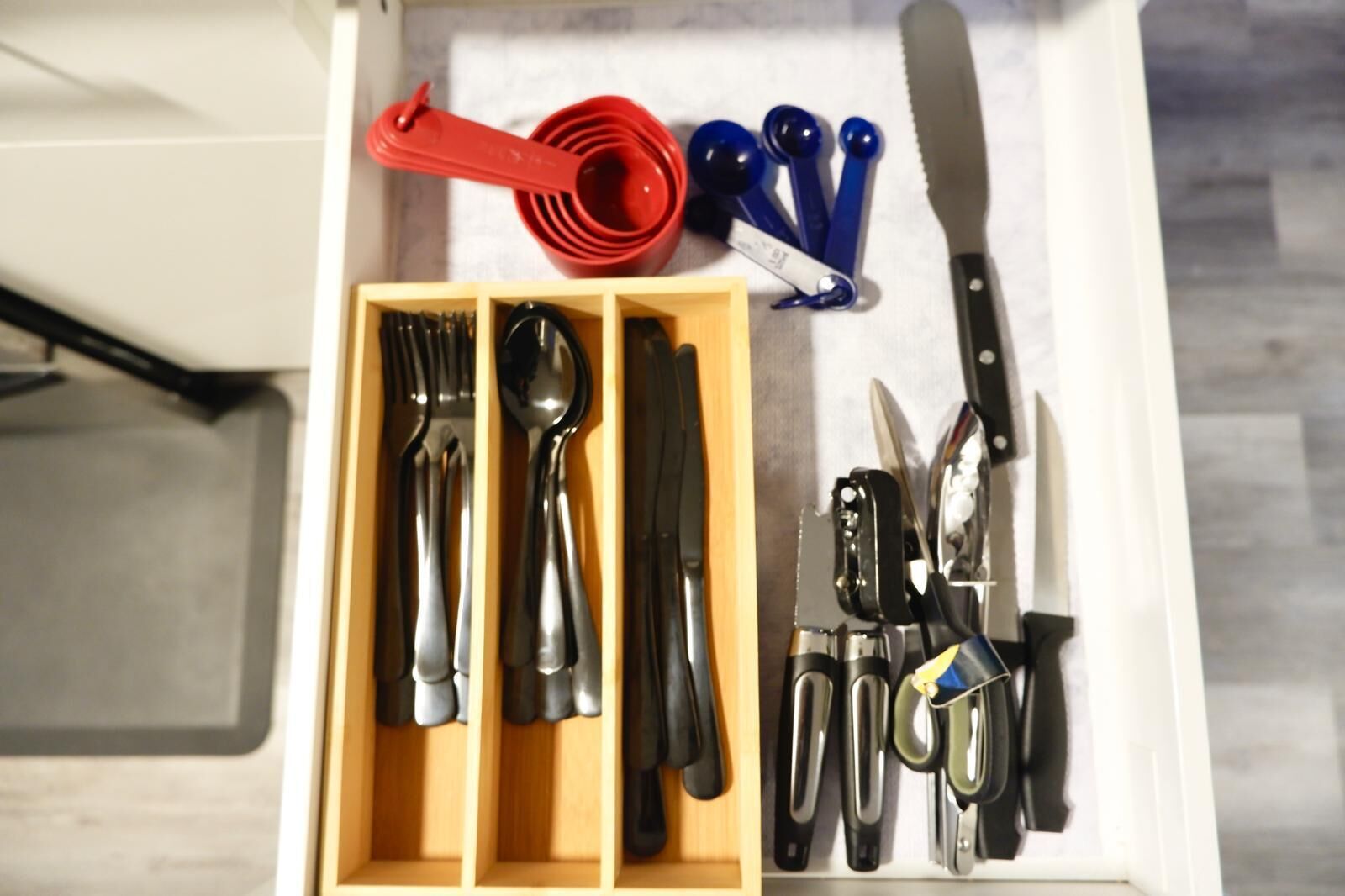 A drawer containing various utensils and kitchen tools, including spoons, forks, knives, and measuring cups.
