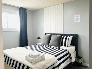 Ein ordentlich bezogenes Bett mit Streifenmuster, eine Nachttischlampe und ein Schild mit der Hinweis auf Ruhezeiten.