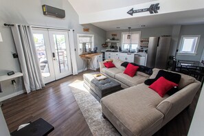 A modern living room with a sofa, ottoman, and a kitchen area in the background.