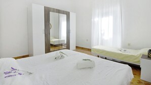 Ett hotellrum med en stor garderob, en säng med ett vitt täcke, ett sängbord och ett fönster med tunna, genomskinliga gardiner.