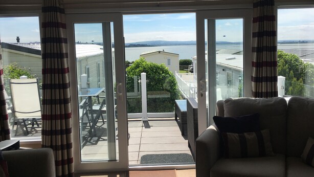 A room with a view of a body of water, a balcony with outdoor furniture, and a sliding glass door. - Iris Lodge, 3 bedroom, dogs stay free at Rockley Park, Poole Harbour, Dorset (Poole)