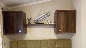 A bedroom with a tufted headboard, two pillows, wooden cabinets, and a shelf with a decorative item. - Iris Lodge, 3 bedroom, dogs stay free at Rockley Park, Poole Harbour, Dorset (Poole)