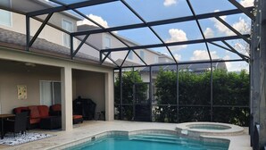 Een zwembad met glazen omheining, een overdekt zitgedeelte met een bank en stoelen, en een jacuzzi.