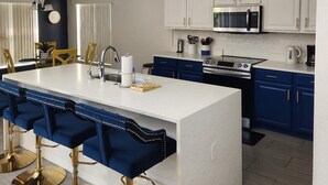 Een moderne keuken met witte kasten, een centraal eiland met barstoelen, en een eethoek met een tafel en stoelen.