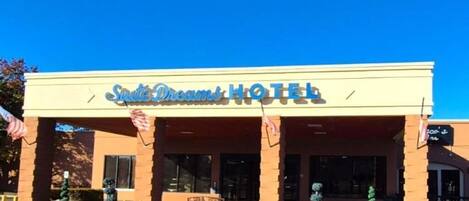 Ein Hotel namens 'Suite Dreams Hotel' mit einem gut sichtbaren Eingang, amerikanischen Flaggen und Blumentöpfen.