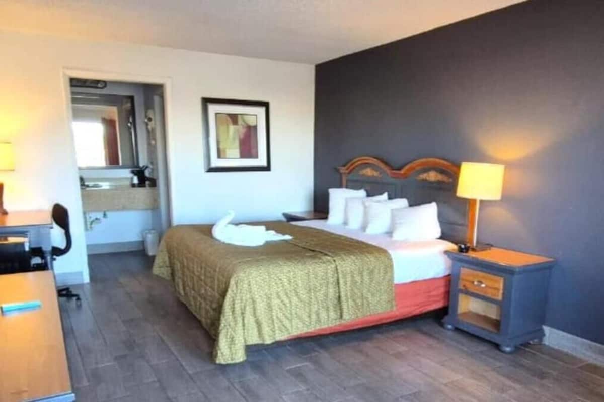 Habitación de hotel con cama, mesita de noche, lámpara y un pequeño escritorio con silla.