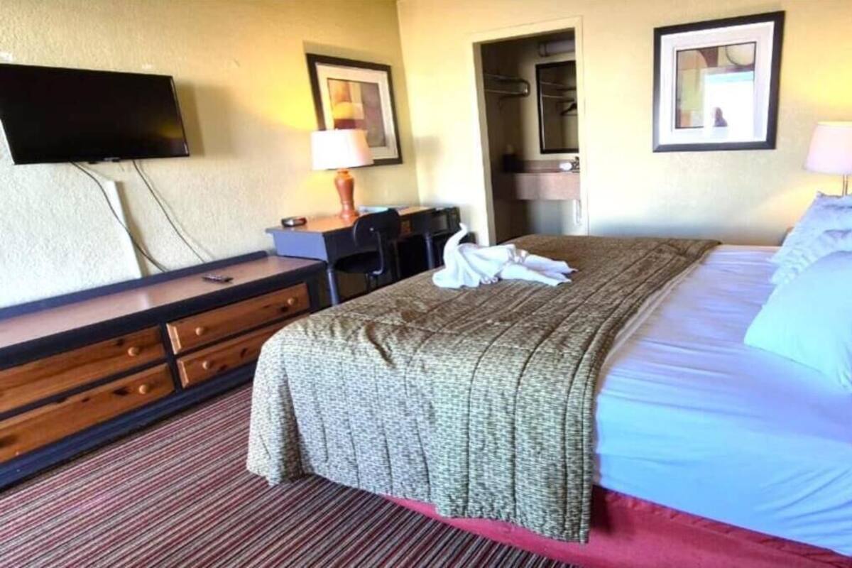 Habitación de hotel con cama, escritorio, silla, televisión y espejo de baño.