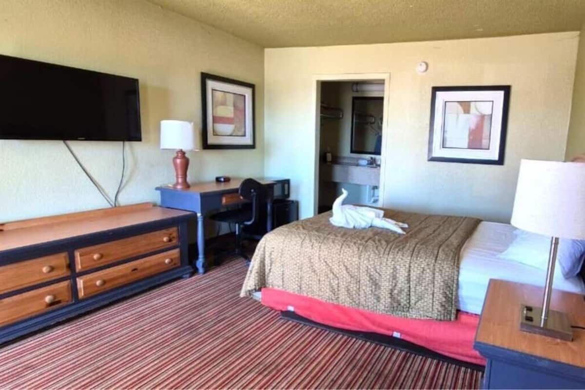 Una habitación de hotel con una cama, un escritorio, una silla, un televisor y un espejo.