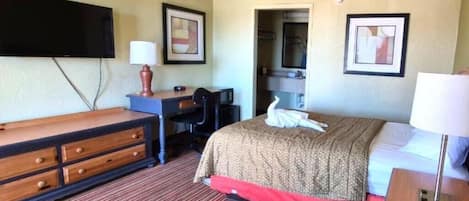 A hotel room with a bed, a desk, a chair, a television, and a mirror.
