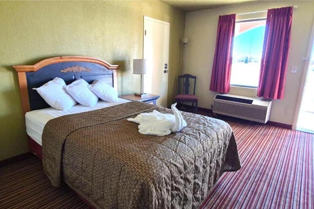 Una habitación de hotel con una cama, una silla, una ventana con cortinas y un equipo de aire acondicionado.