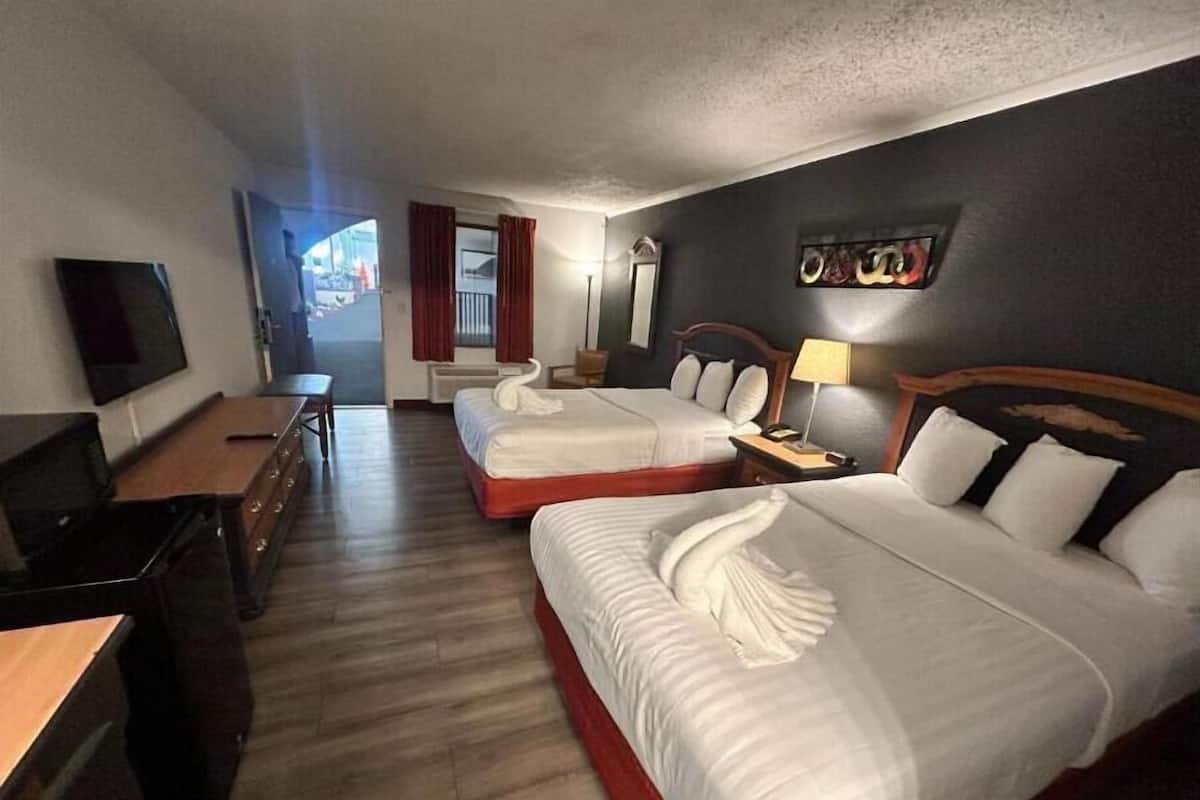 Habitación de hotel con dos camas, un escritorio, televisión y ventana con cortinas.
