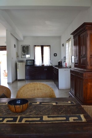 A compact kitchen with a refrigerator, microwave, and stove. There is a dining table with a woven table runner and a bowl.