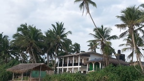 Ein Strandgrundstück mit einer strohgedeckten Struktur, einem mehrstöckigen Gebäude mit Balkonen und Palmen.