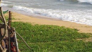 Ein Strand mit Wellen, ein felsiges Ufer mit Booten und ein Schiff in der Ferne.
