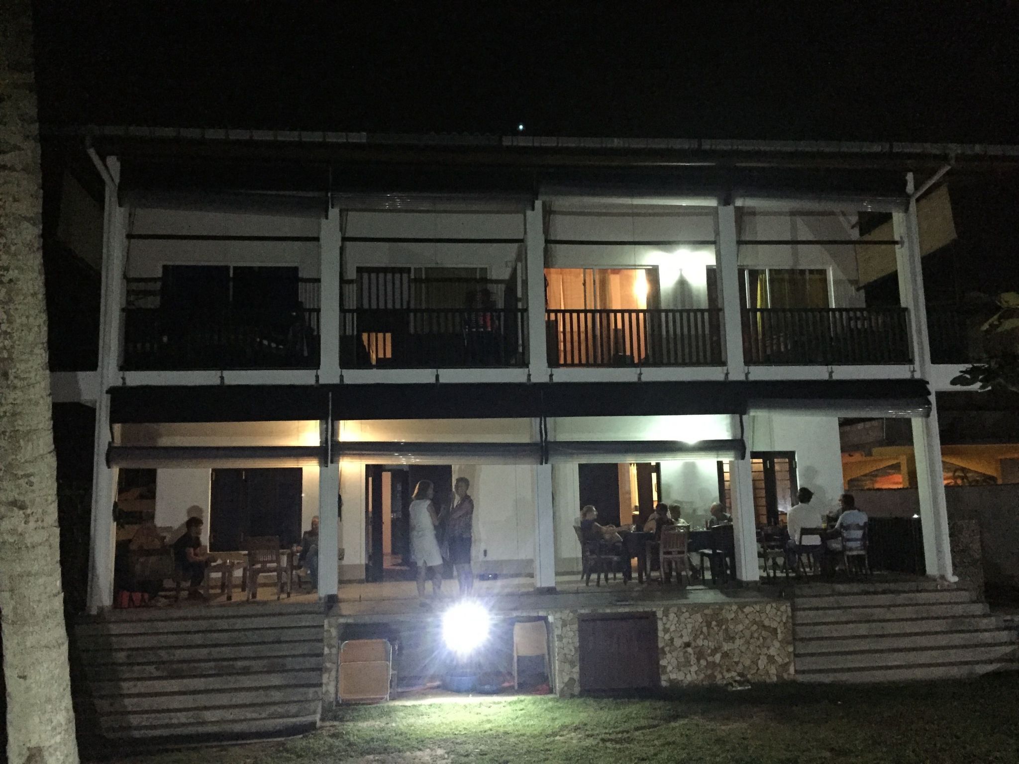 Een gebouw met twee verdiepingen, een balkon op de bovenste verdieping, terrasplekken en een goed verlichte ingang.