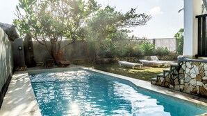 Ein Pool mit Steinmauer und Liegestühlen.
