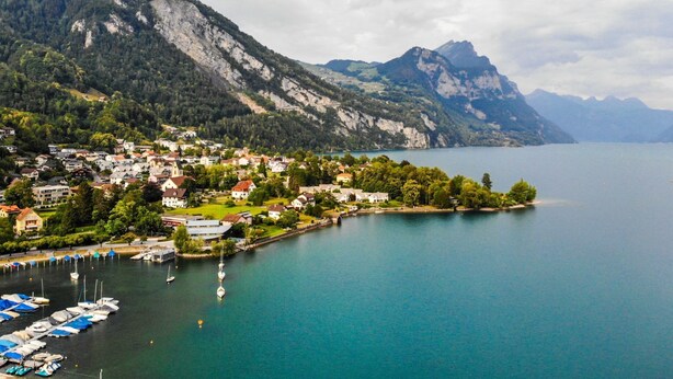A lakeside town with houses, a marina, and mountains in the background.
