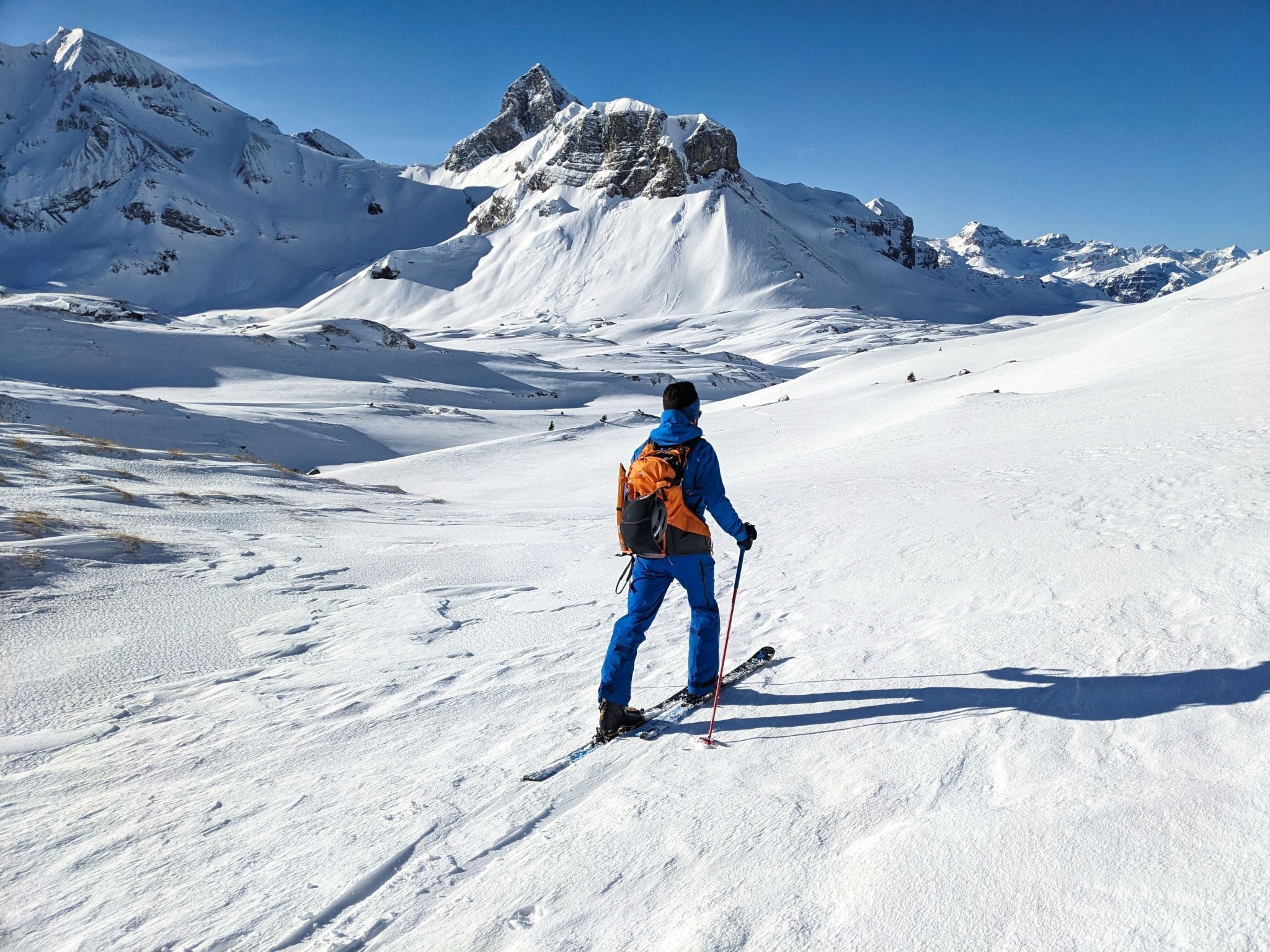 Eine Person fährt Ski eine schneebedeckte Piste, im Hintergrund ist ein Berg zu sehen.
