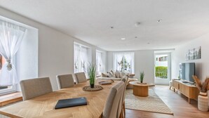 A modern living room with a wooden dining table, sofas, a TV, and a balcony view.