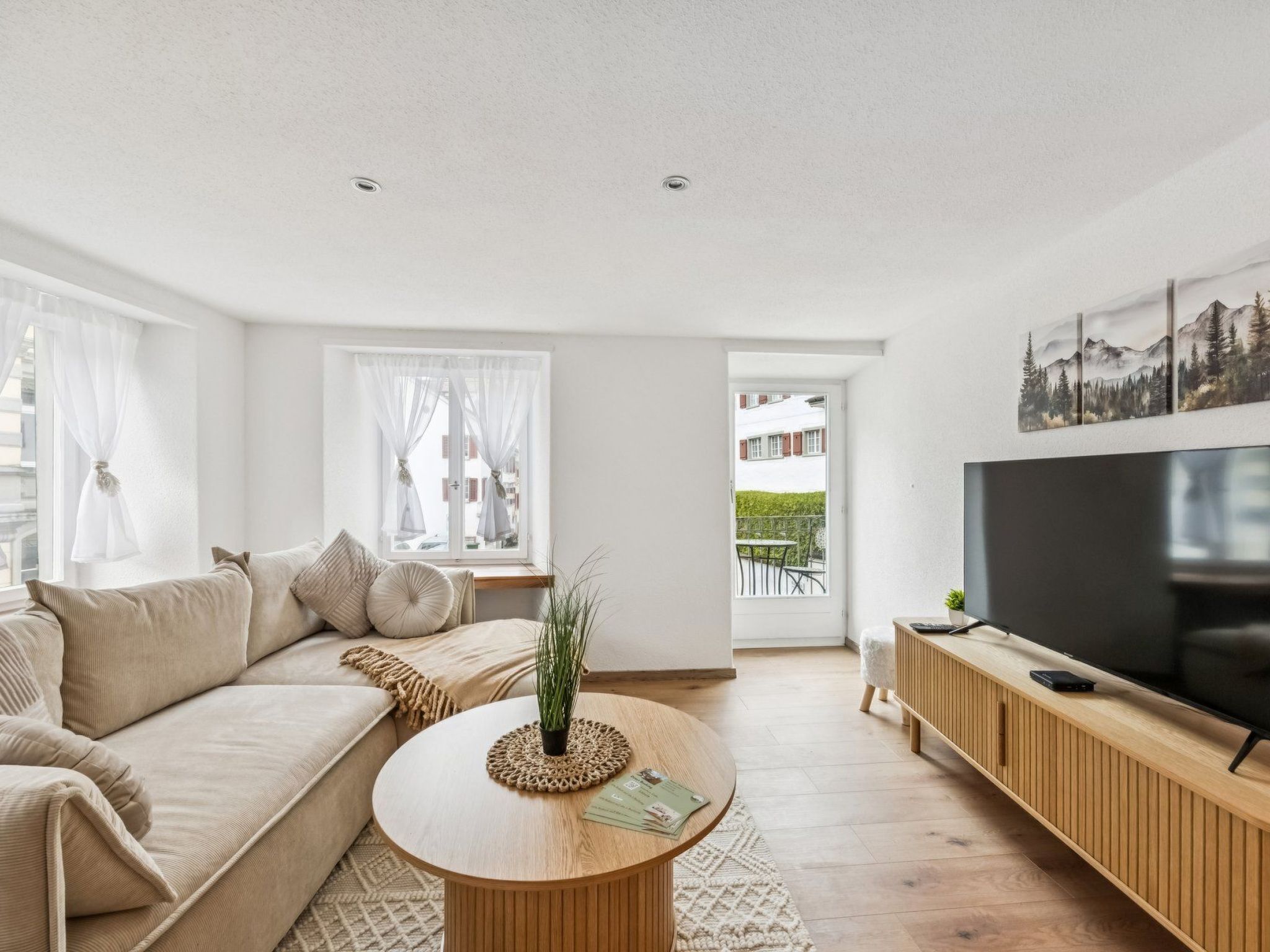 Un salon moderne avec un canapé, une table basse ronde, un téléviseur et une vue sur l’extérieur.